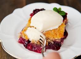 A slice of berry cobbler topped with vanilla ice cream on a white plate.